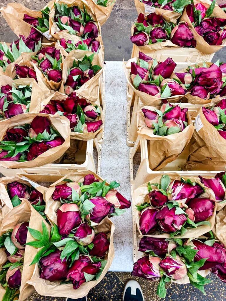 Purple peony flowers in wrapped in brown paper are stacked on the sidewalk.