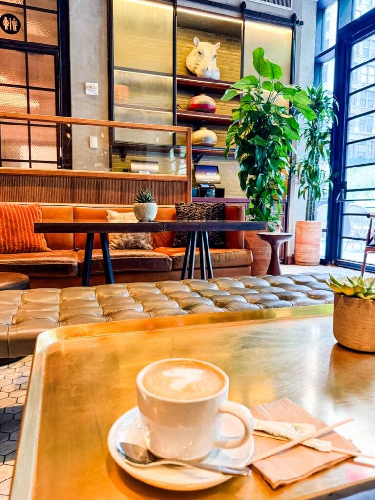 A cappucino is served on the table in front of a long couch at the Back Bar inside the Kimpton Hotel near the NY Flower Market.