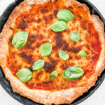 pizza in skillet with fresh basil leaves on top
