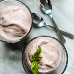 2 glass cups of strawberry basil ice cream with fresh basil in one and 2 small spoons