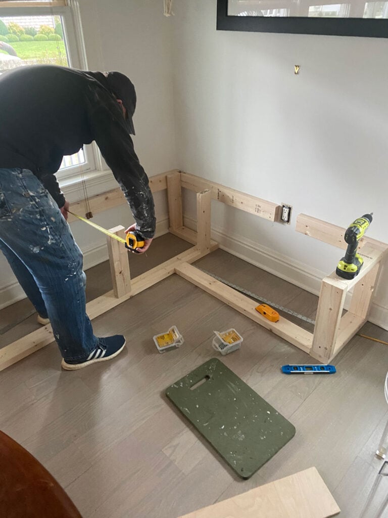 A man is measuring to build a top piece for a custom corner banquette.