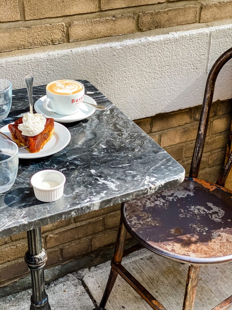 A small outside table at Buvette in New York City. A tarte tatin and a cappuccino are on the table.