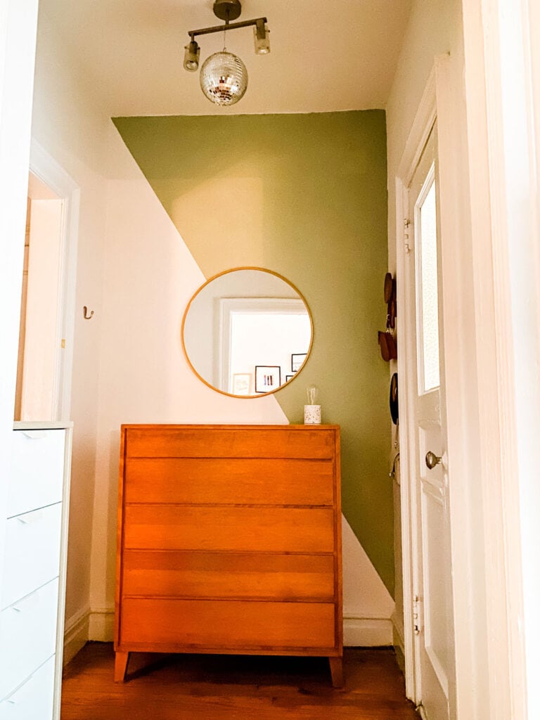 A painted wall, a round mirror, and a dresser in the dressing area of a studio apartment in Brooklyn, NY.