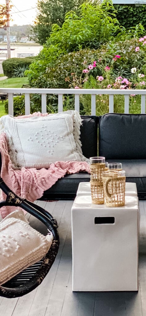 Pink throws on a black outdoor sofa with glasses and a pitcher on a coffee table and the harbor in the background.