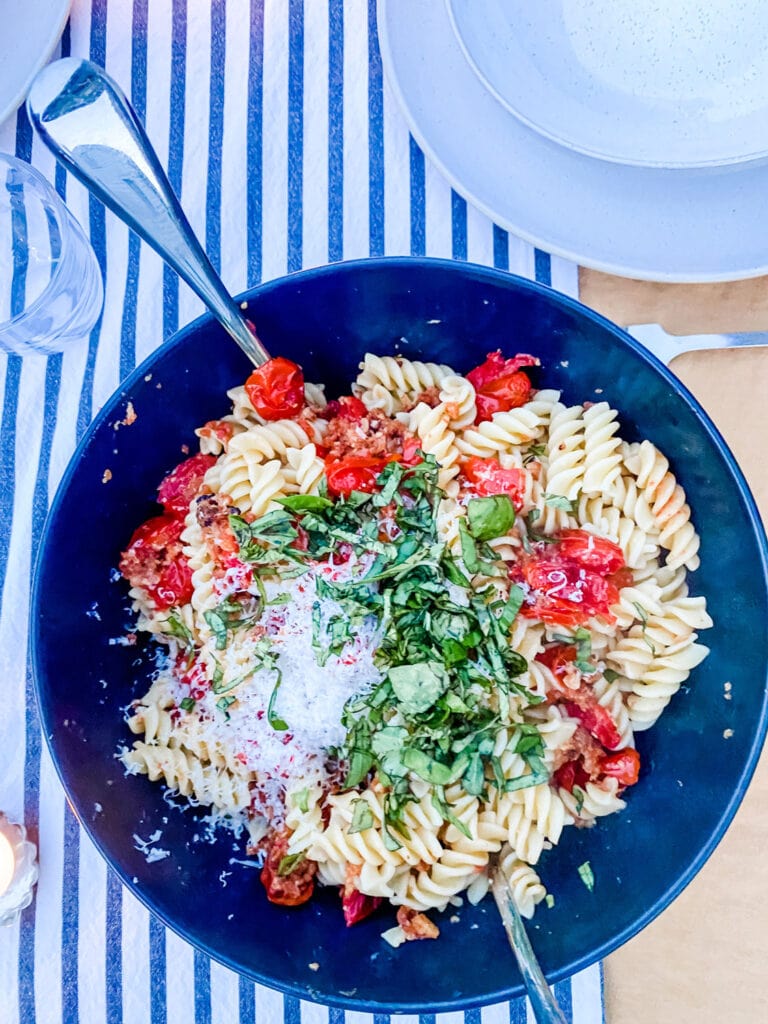 Summer corkscrew pasta with cherry tomatoes is in a large black bowl and served family style. It's on a table with a french blue and white striped table cloth.