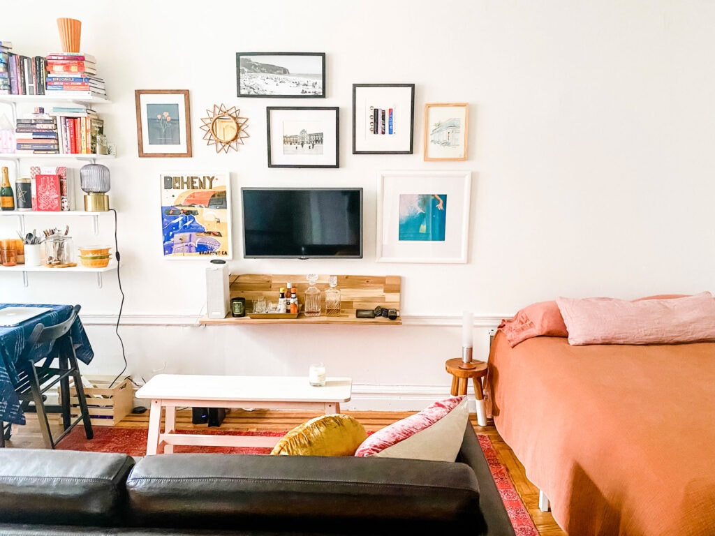 A gallery art wall in a small studio apartment. Off to one side is the bed and on the other side are shelves for storage.