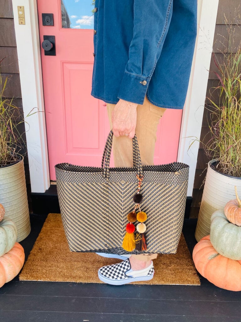 woman holding market bag with pom moms in front of a pink door 