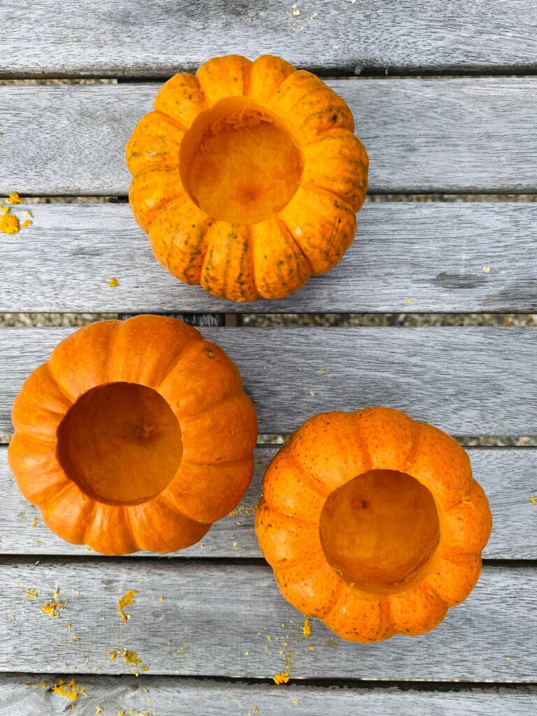 Three mini pumpkins that have carved out into plant holders sitting on a wood potting bench.