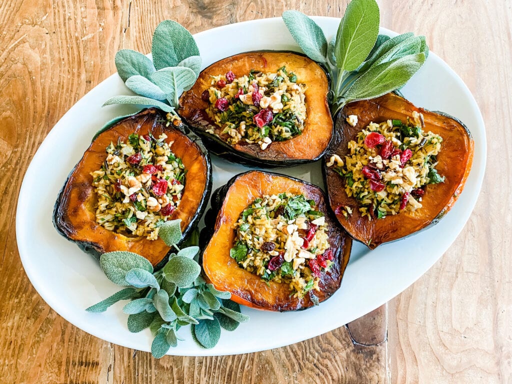 Four acorn squash halves are stuffed with wild rice and served on a large, white platter with fresh sage leaves.