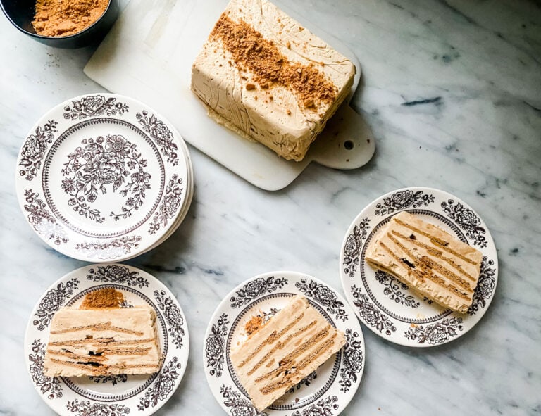 gingerbread icebox cake on brown and cream patterned plates with cake on white marble board with cookie crumbs on top