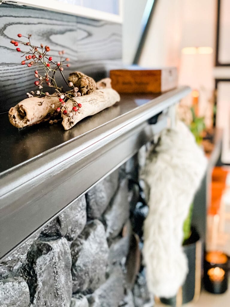 Foraged red berries and driftwood from the beach add a nice Christmas touch to a black fireplace mantel. A vintage cigar box is in the background.