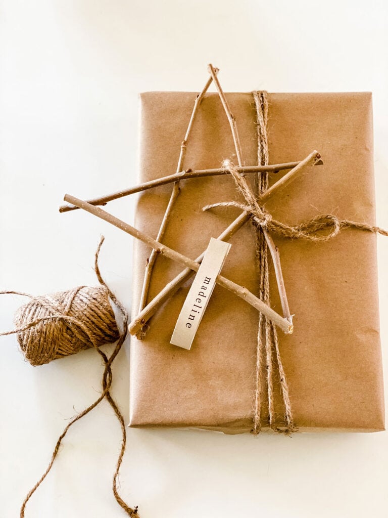 A twig star as a name tag on a present wrapped in a brown kraft paper bag. Twine is used to fasten the star to the present.