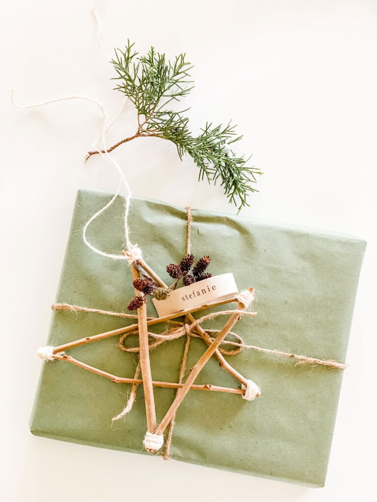 A present is wrapped in green kraft paper and natural twine. A twig star and a piece of evergreen are used for additional decorations.
