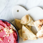 black bowl of pink beet hummus with pita bread on white marble
