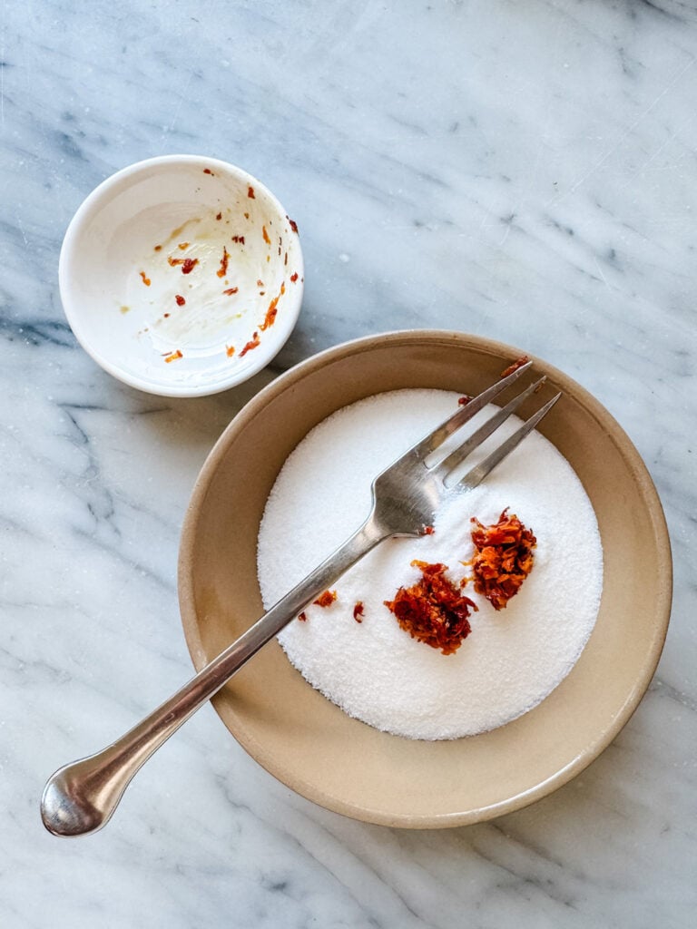 Blood orange zest is in a bowl of granulated sugar.