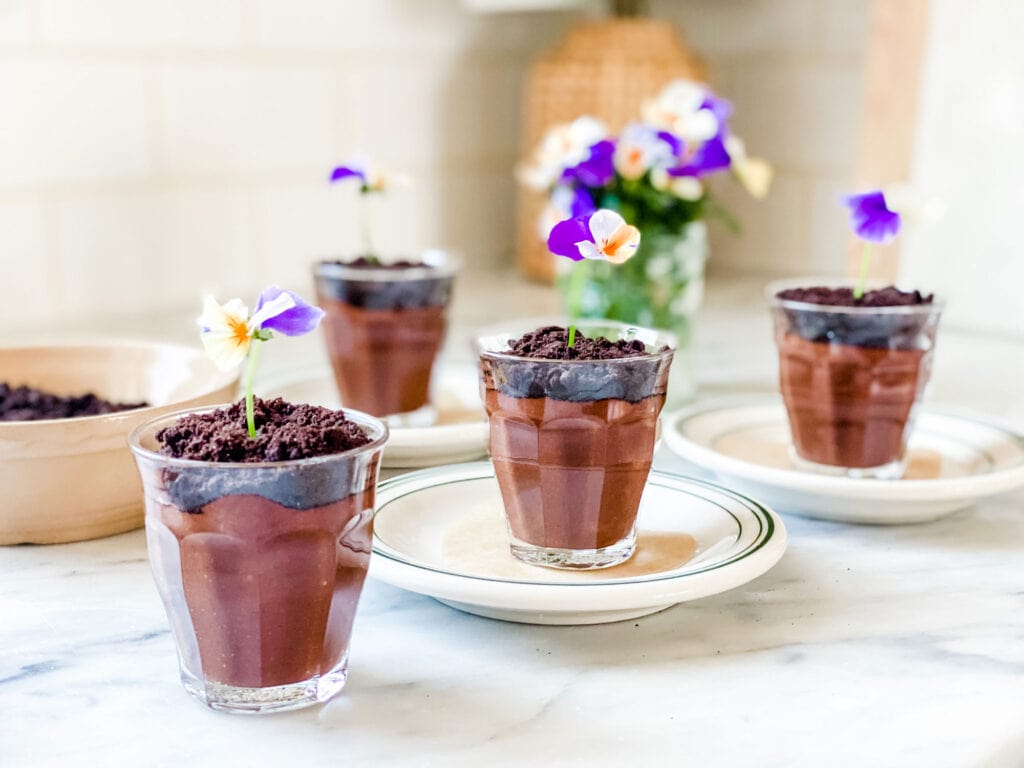 Small serving glasses of Chocolate Budino, crush chocolate cookie crumbs, and edible flowers.