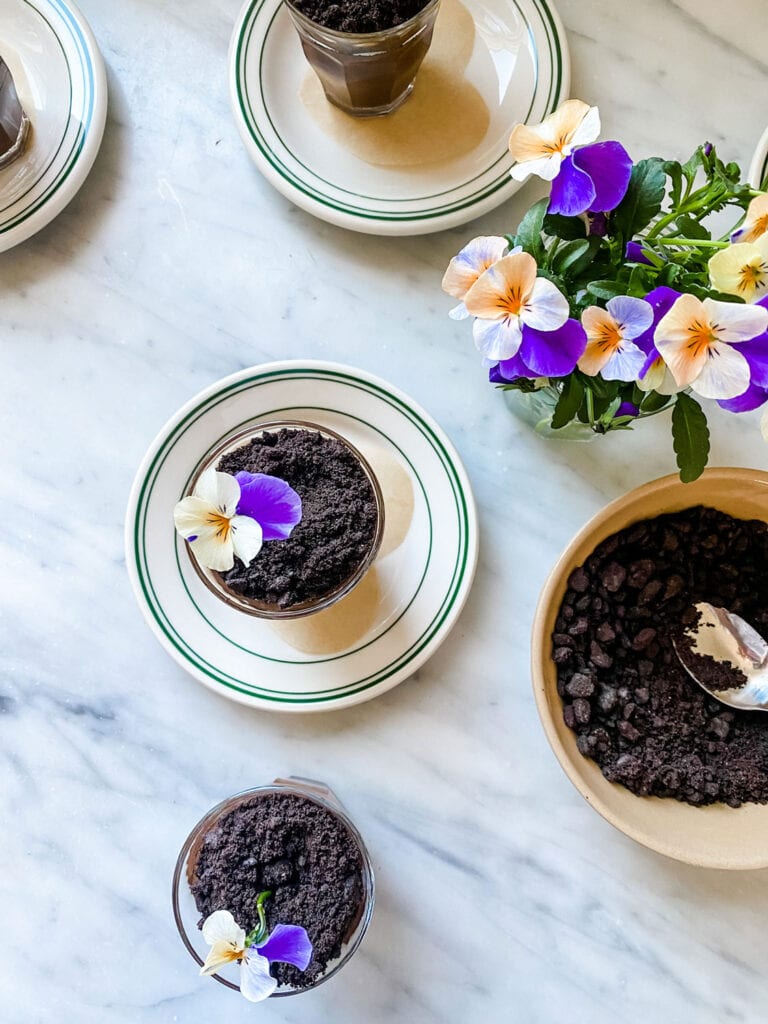 Chocolate Budino in small glasses with cookies crumbs that resemble dirt and edible flowers on top.