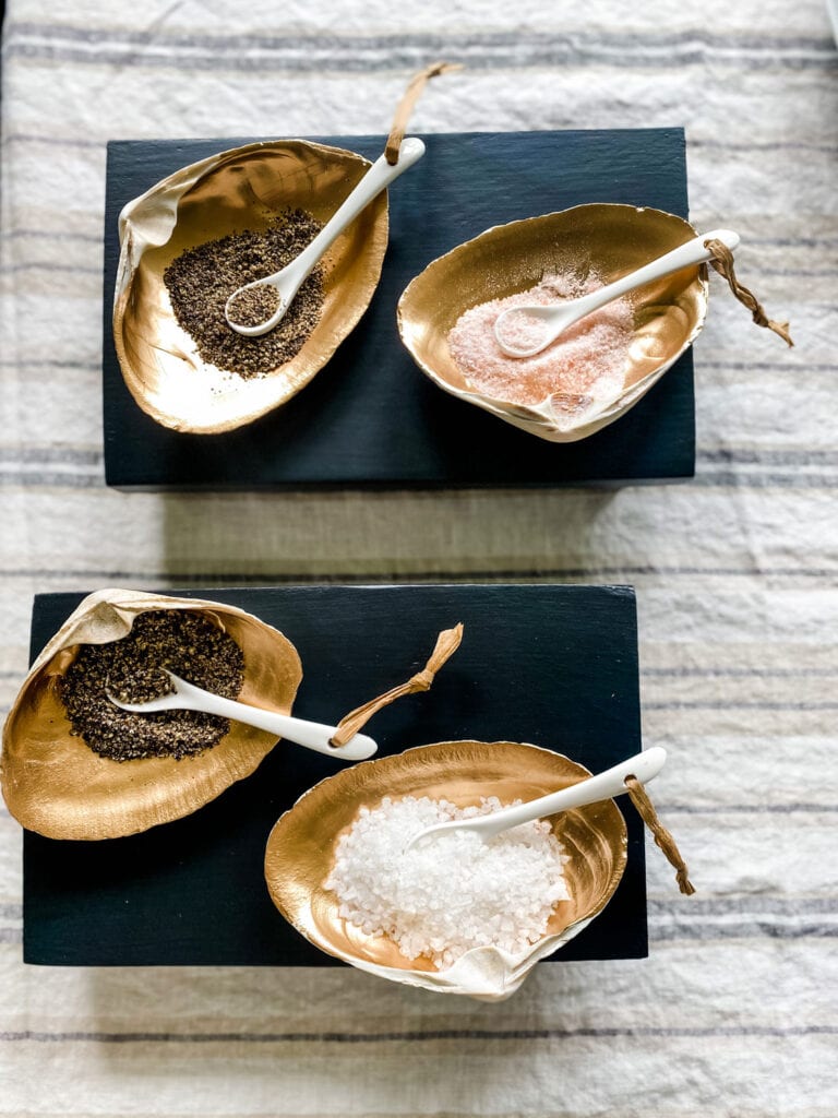 Gold leaf clam shell salt cellars with porcelain spoons are sitting on small black trivets.