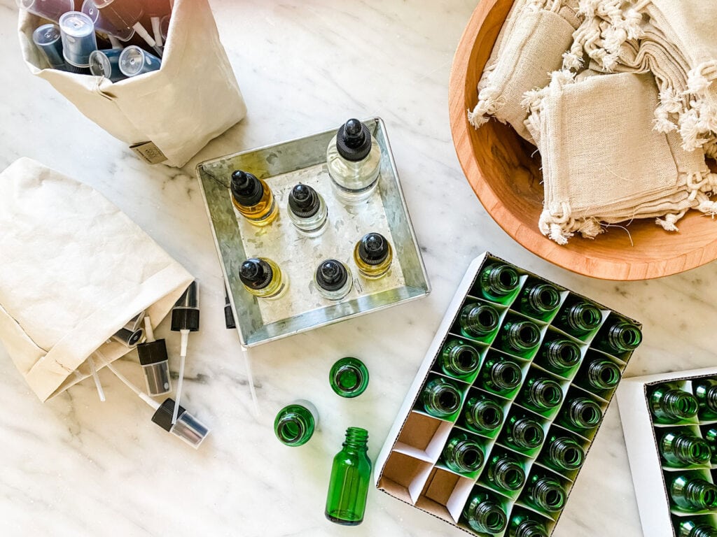 Small green bottles, cloth sachets, essential oils on a silver tray, spray tops for green bottles and a cloth bag of supplies for making bug spray.