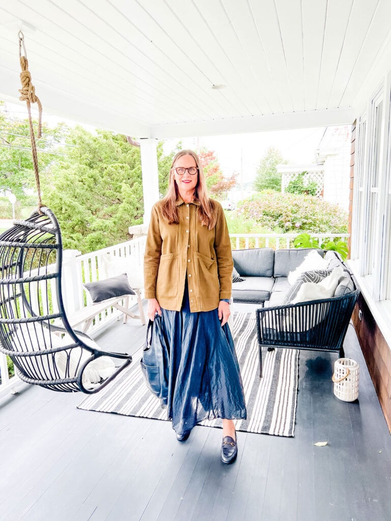 A woman standing on the porch of a coastal Connecticut home wearing a brown chore coat, black skirt and black Gucci loafers