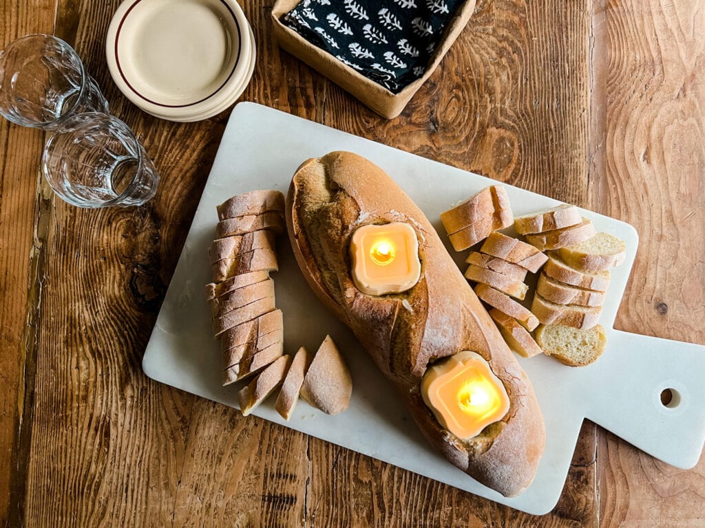 Two garlic butter candles are cut into and placed in an Italian loaf of bread. Around it are slices of a fresh baguette ready to be served.