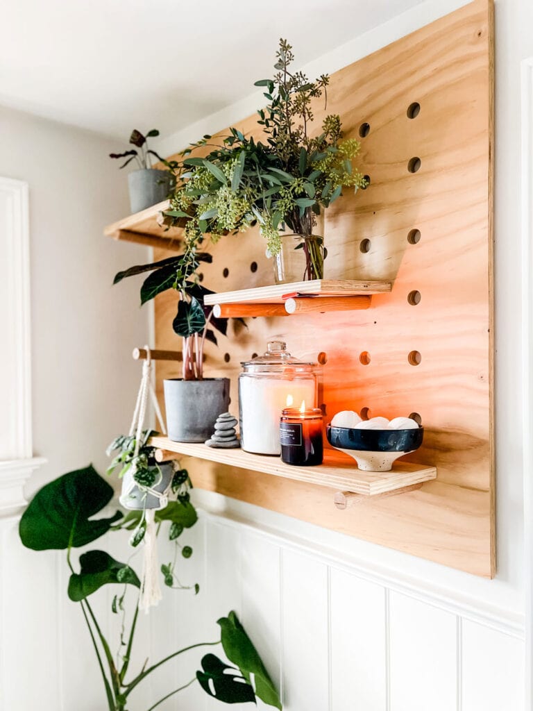 A plywood pegboard in the bathroom displays plants, Epsom salts and a candle