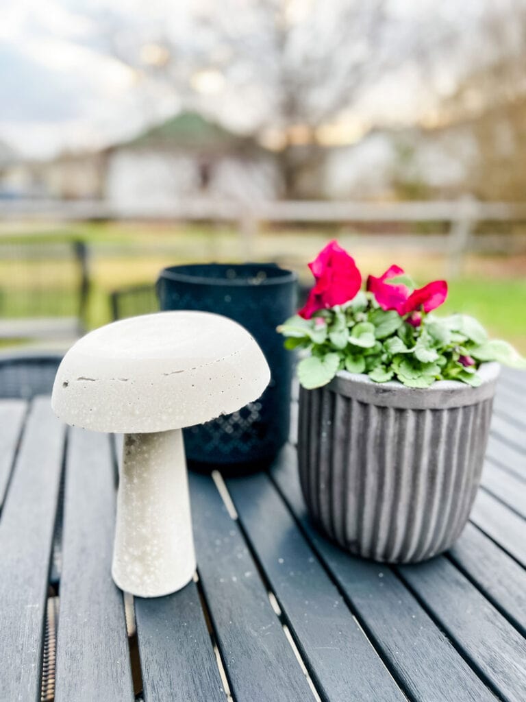 A cement mushroom next to a spring plant in a Bergs pot.