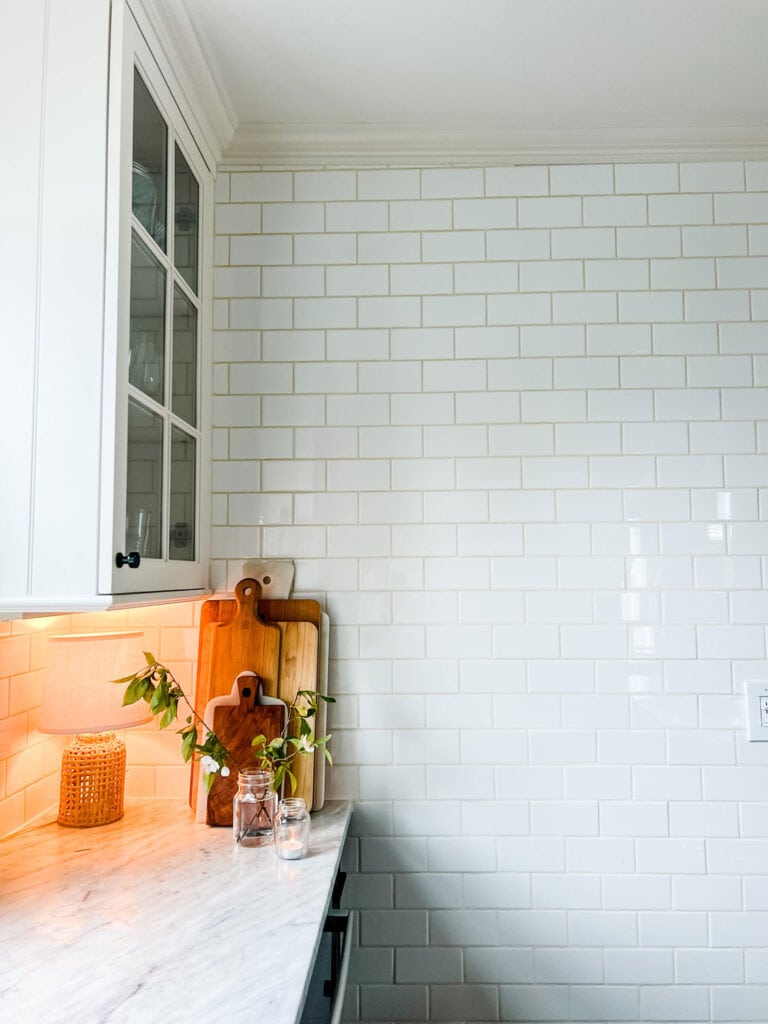 A few small branch clippings are in several glass jars sitting on a kitchen counter in front of a wall of white subway tiles.