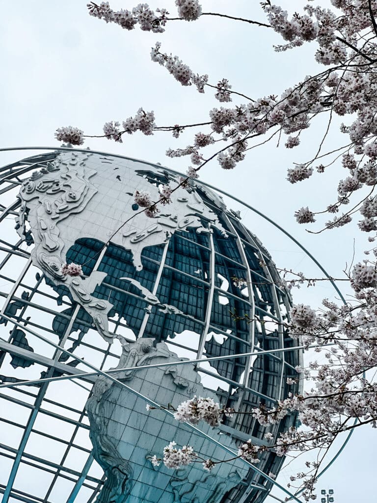 Cherry blossoms in front of a close-up of the Unisphere at Flushing Meadows Corona Park.