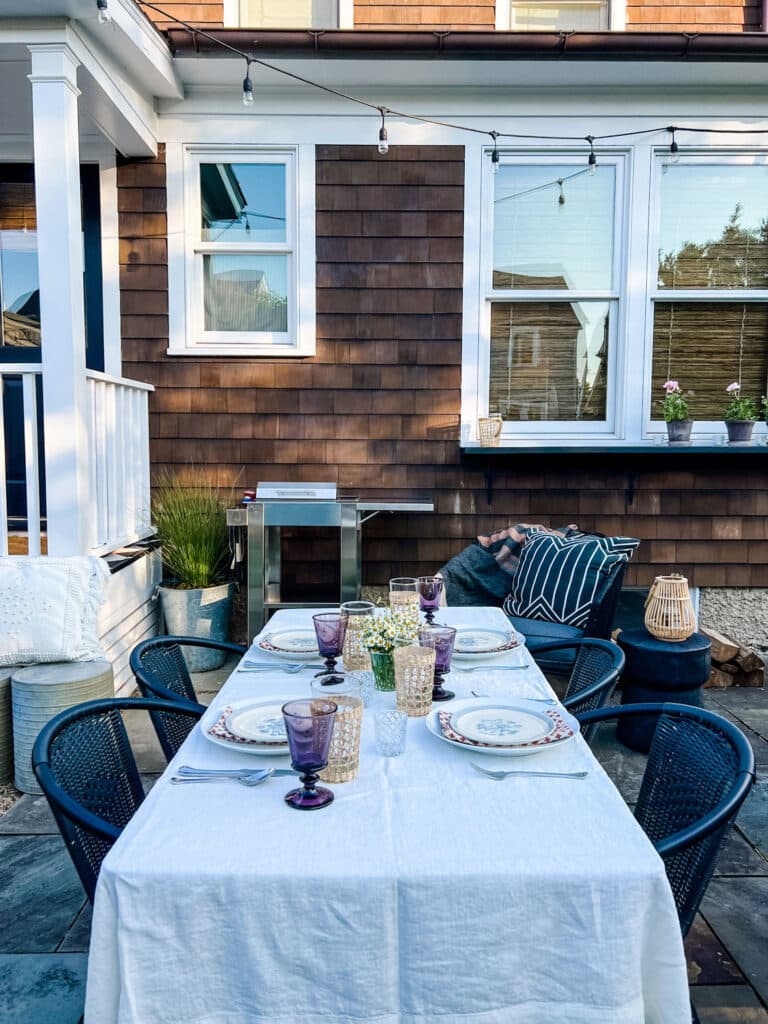 table set with dishes, glassware, grill, potted pants in backyard patio area