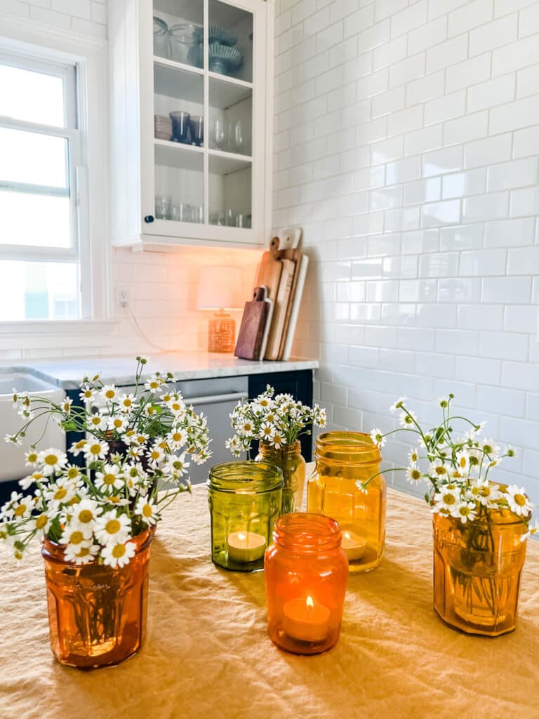 tinted glass jars on gold linen cloth in kitchen with flowers and tea lights