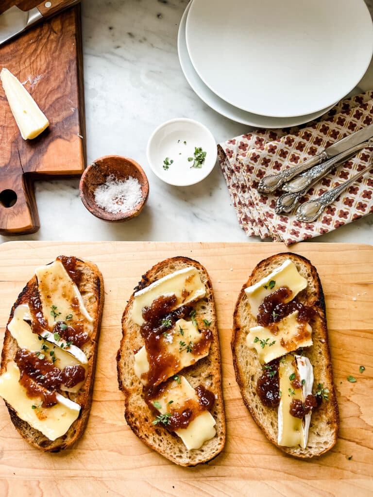 Make this Easy & Delicious Creme Brûlée Brie Tartine, 3 slices of toast with Brie cheese, jam, thyme on wood cutting board