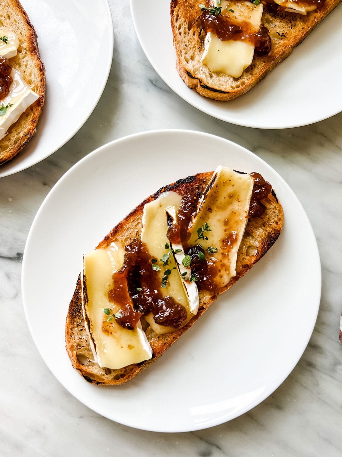 Toast with cheese, fig jam and fresh thyme on white plates