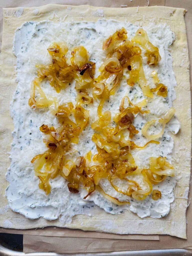 Caramelized shallots are spread evenly on the goat cheese and puff pastry sheet.