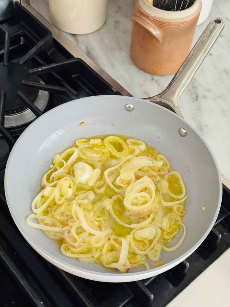 Onions in olive oil are being caramelized in a non-stick pan.