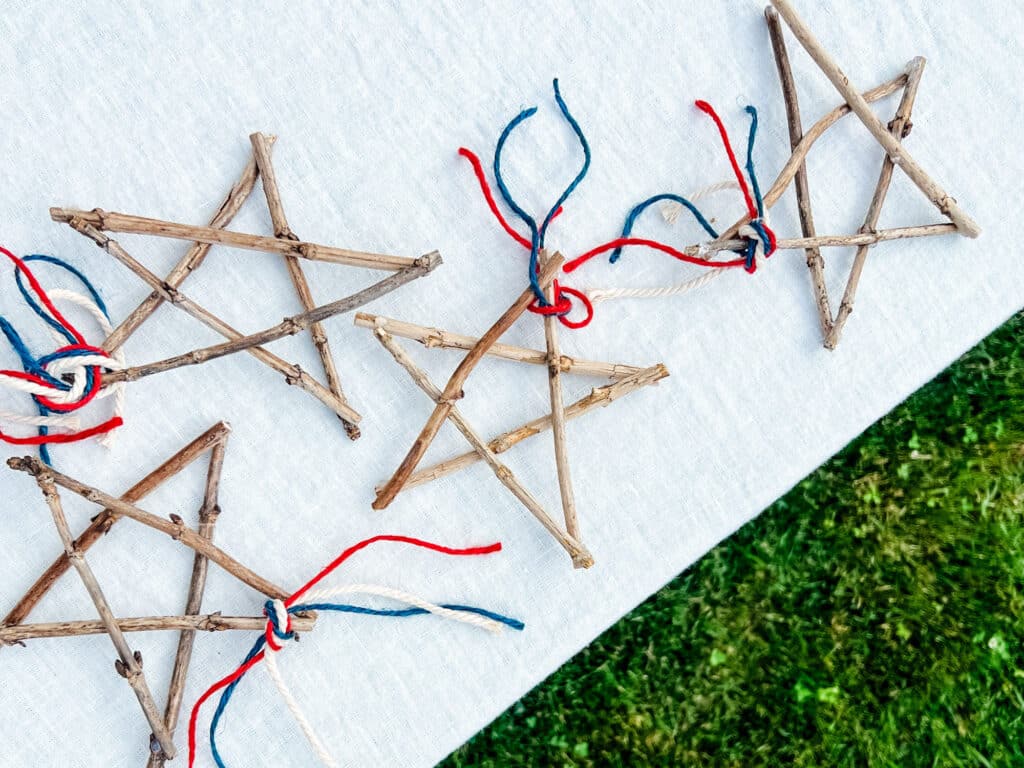 Make Easy DIY Hydrangea Twig Star Decorations - Twig stars with red and blue jute twine on white tablecloth next to grass 