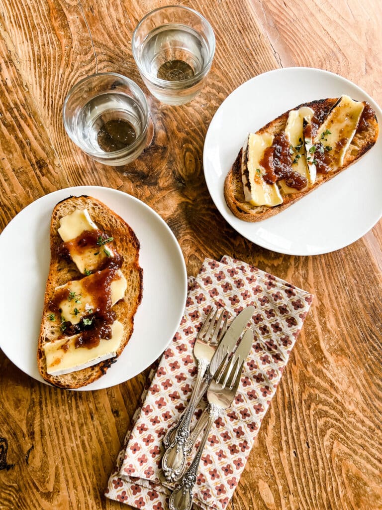 Make this Easy & Delicious Creme Brûlée Brie Tartine on white plates on wood table, with print napkins and silverware