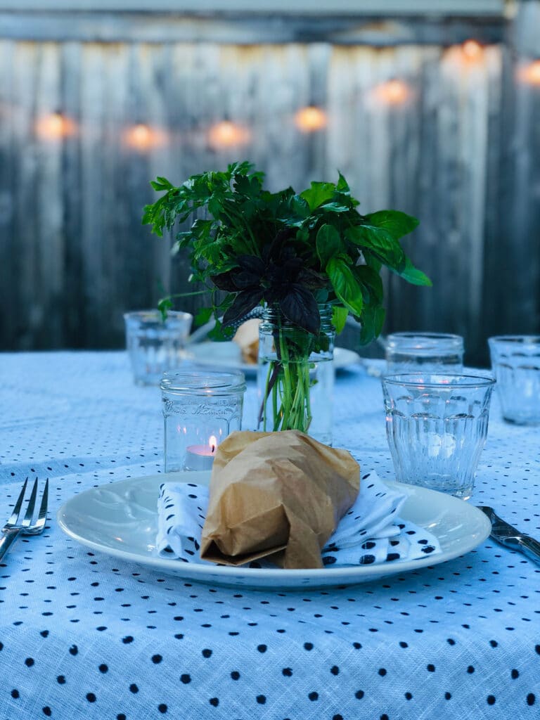 Outdoor table with black and white polka dot table cloth, bread on plate, clear glassware, herbs on table 