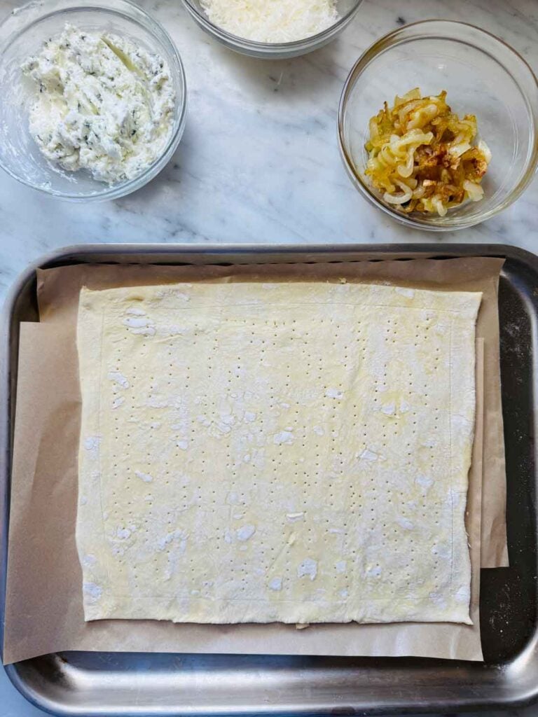 One pastry sheet has been rolled out on parchment paper on a large baking sheet.