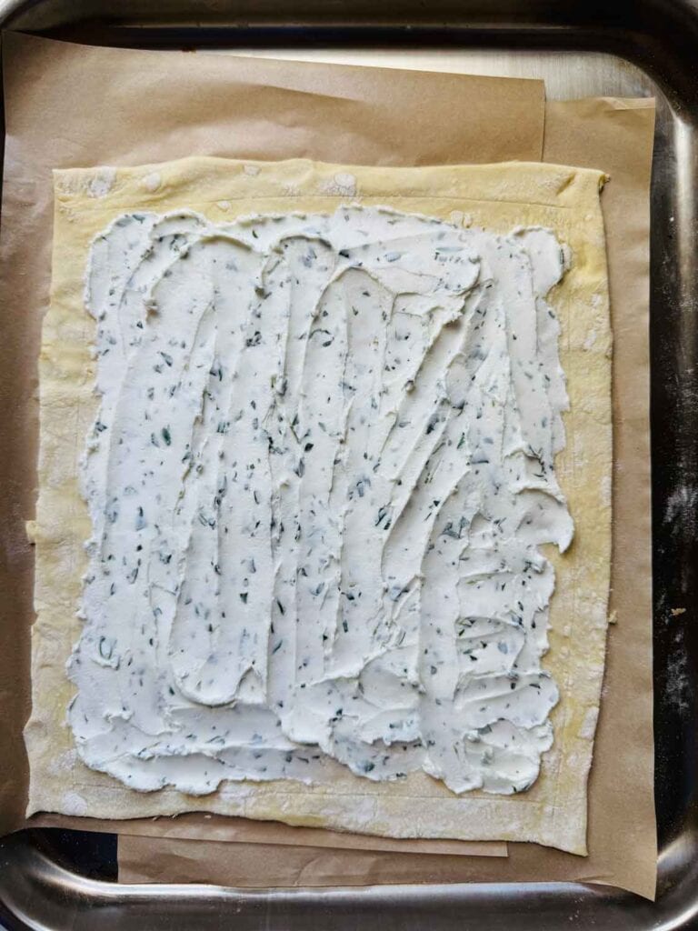 Herbed-goat cheese is spread on a puff pastry sheet right up to the scored edges.