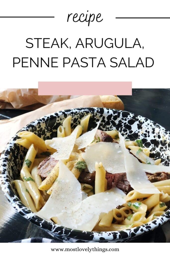 steak penne arugula pasta salad in black and white bowl with shards of parmesan cheese
