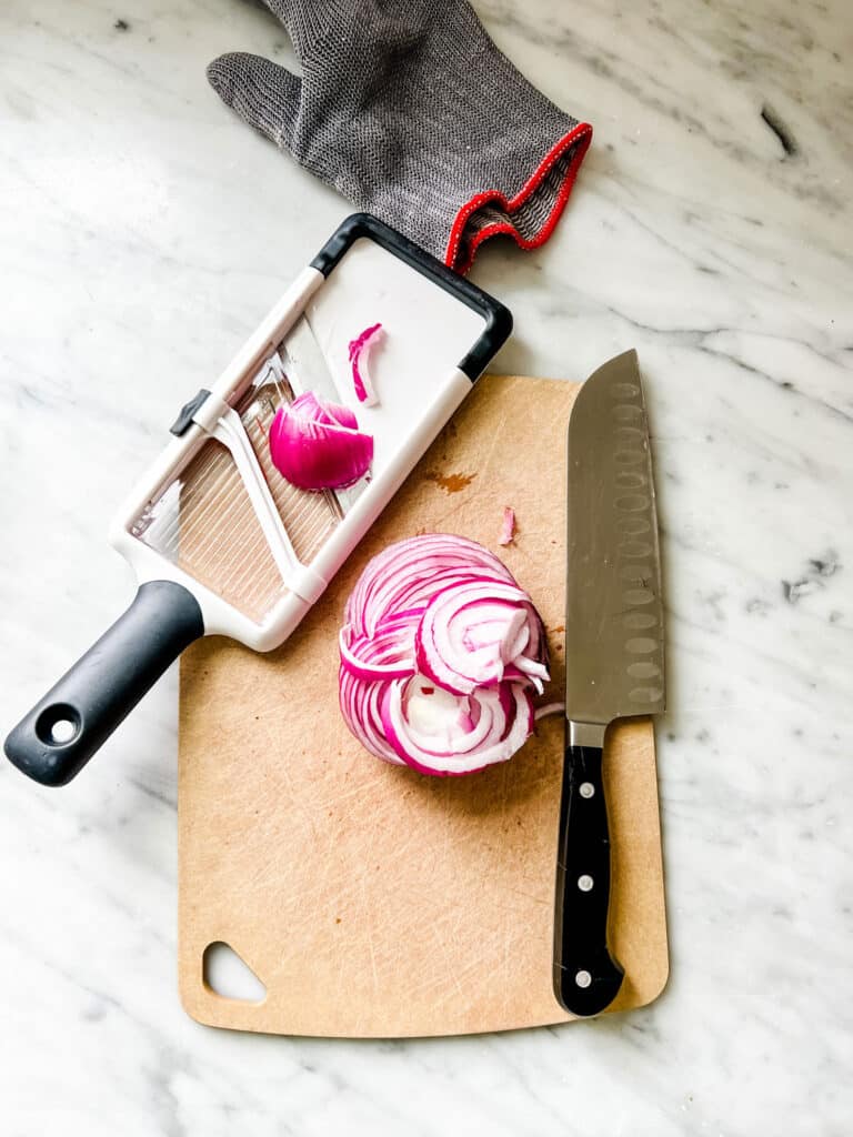 red onion on cutting board, with knife, Mandolin and knife glove
