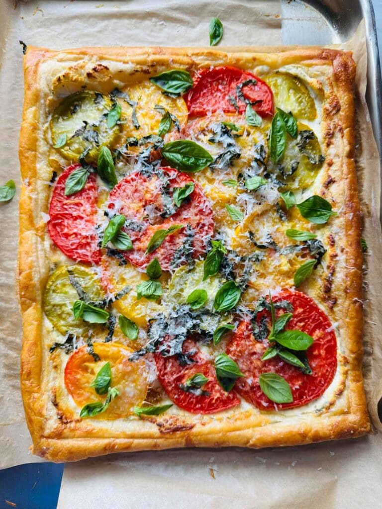 A baked puff pastry tomato and goat cheese tart is on a parchment paper-lined baking sheet.