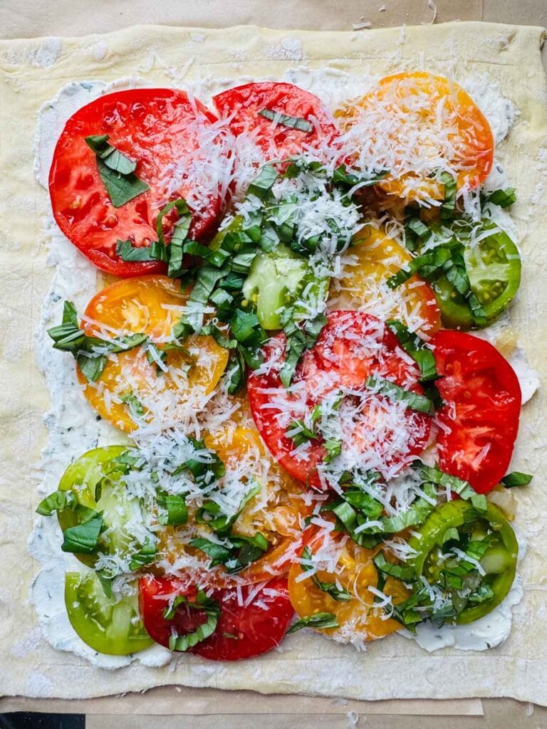 A variety of fresh tomatoes are laid on top of the puff pastry, herbed goat cheese, and caramelized shallots and are topped with with a sprinkle of parmesan cheese.