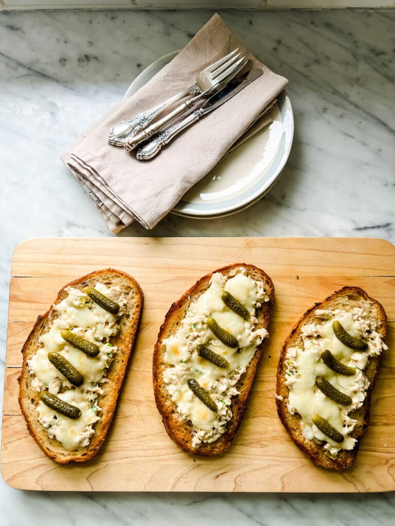 plates, napkins, silverware, open faced sandwiches on cutting board 