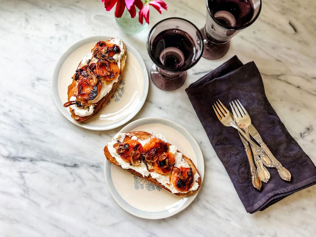 tartine with apricots on plates, with 2 wine glasses, forks, knives, black napkins. flowers 