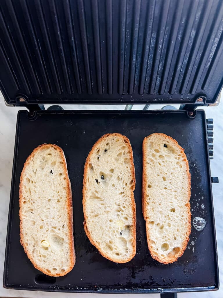 Fresh slices of buttered bread being toasted on a panini maker.