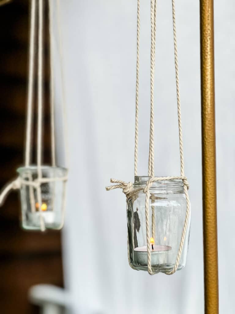 Jars hanging from an over-the-table rod using a DIY macrame jar sling. Candle votives are burning inside the jars. 