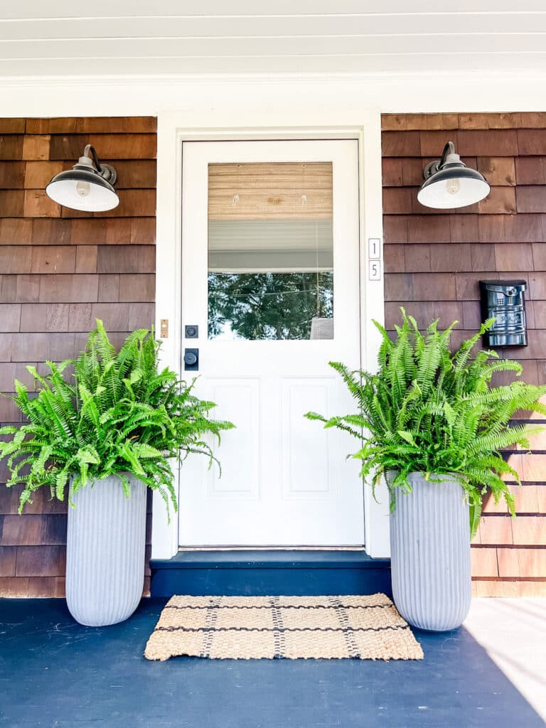 Porch in foreground showing white front door with smart locks from Emtek and on the side large succulent ferns in Terrain pots