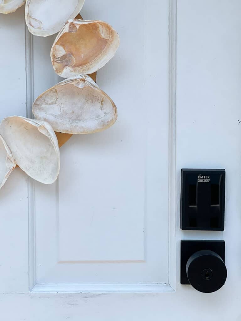 Close up of white side door of house featuring smart keypad from Emtek and shells hanging on door